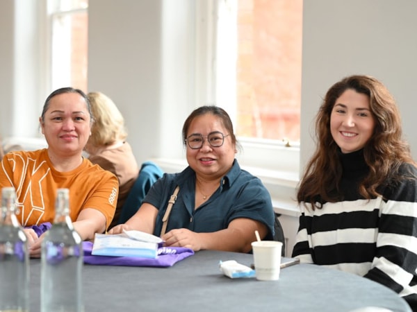3 members at a conference sitting at a table facing the camera and smiling